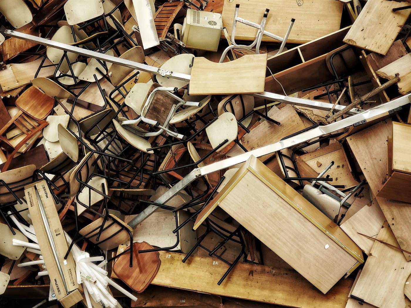 A large heap of stripped-out office and classroom furniture: stacked chairs, desks and table frames