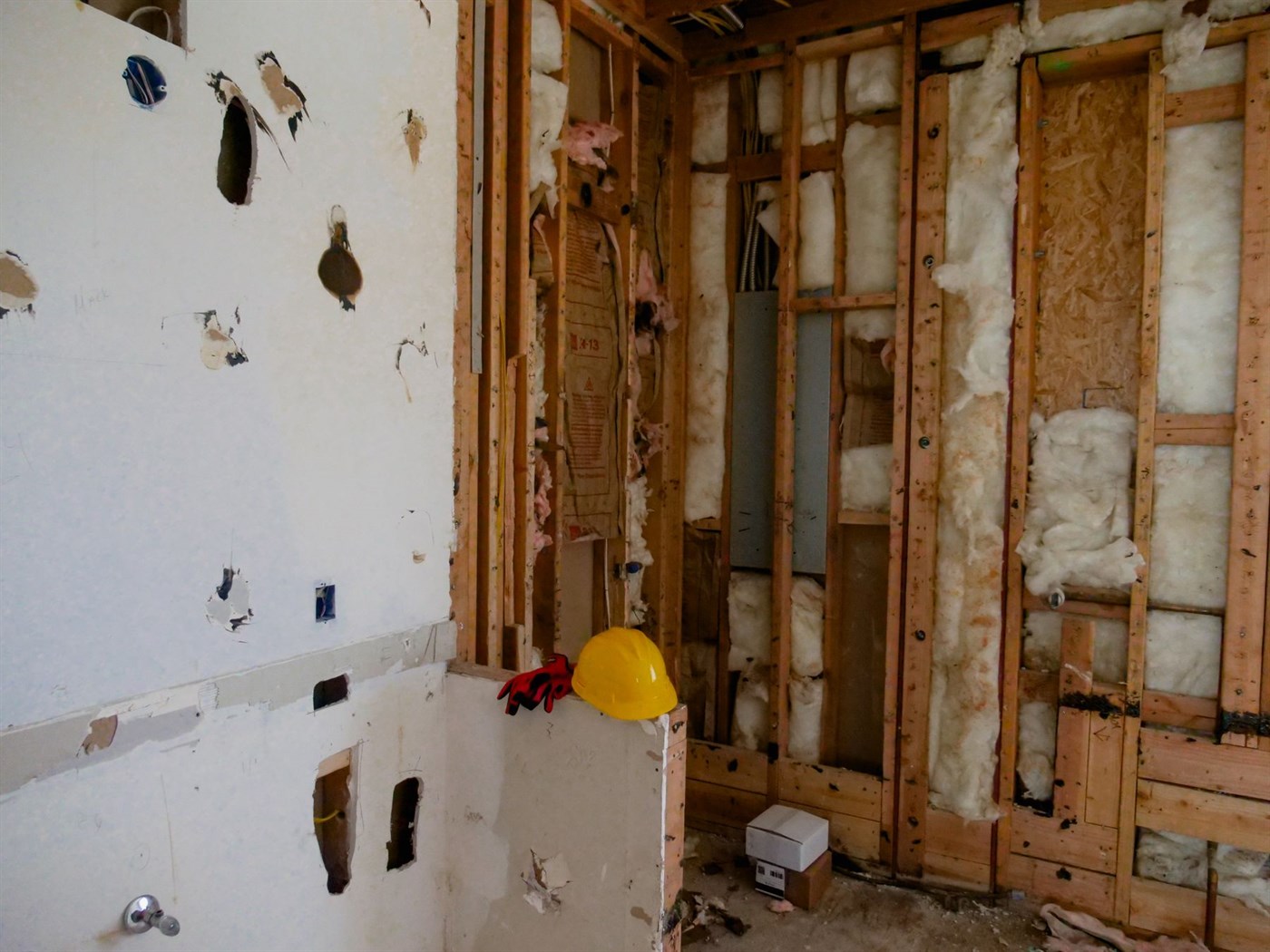 A room mid-renovation with drywall torn back to the studs, exposed insulation and a hard hat resting on a partition