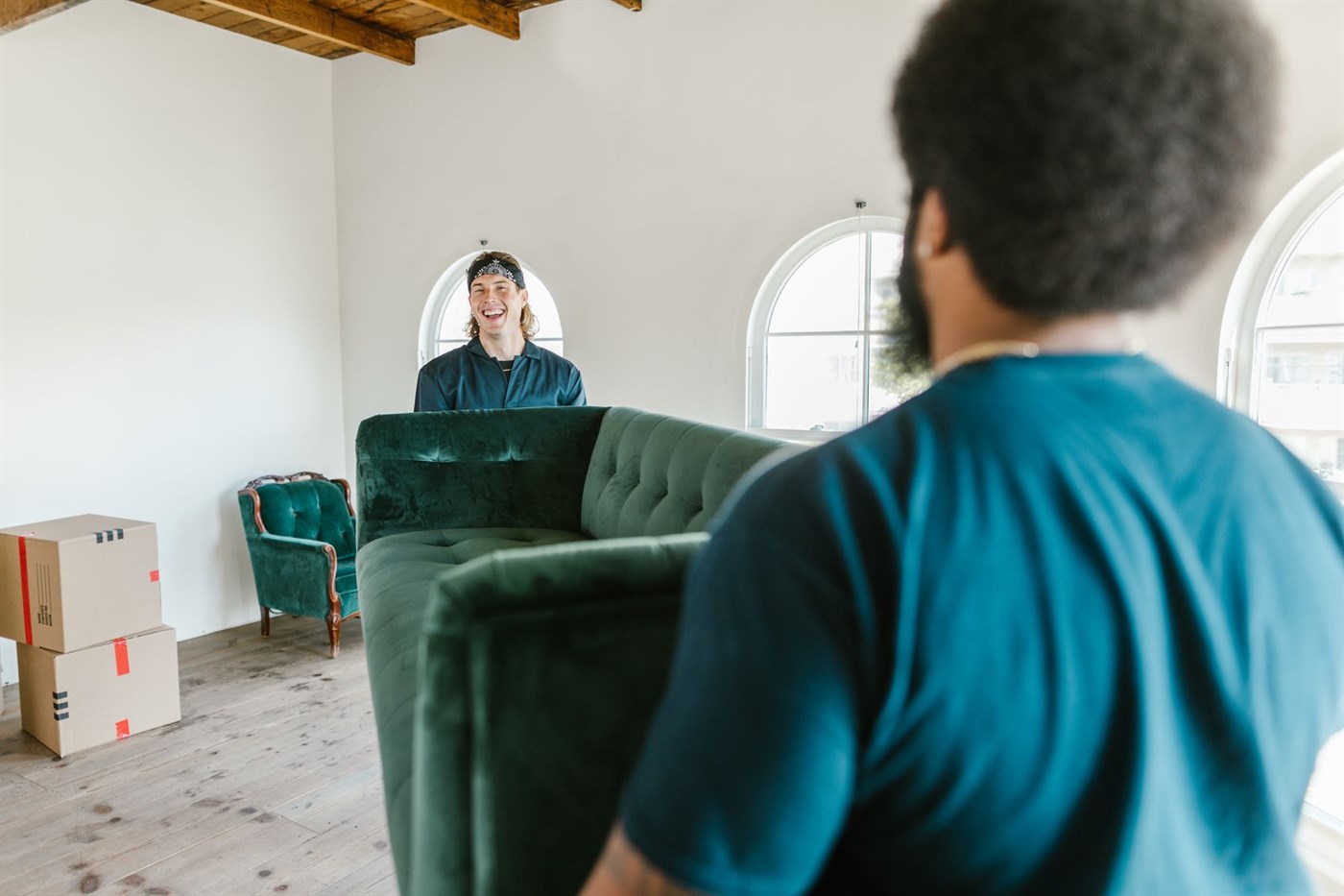 Two people carrying a large sofa out through a bright, emptied room